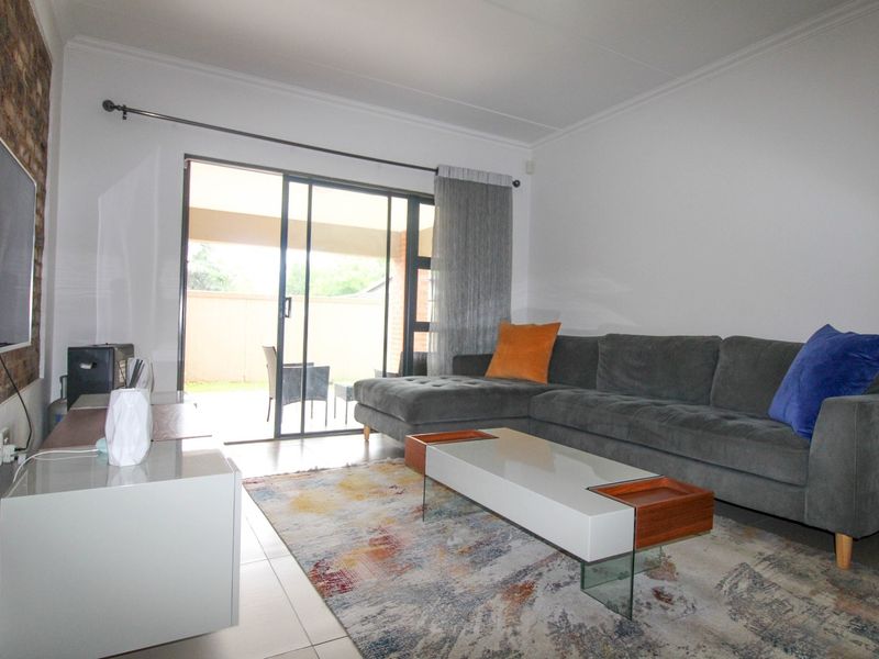 A bright living room featuring tiled flooring, an exposed brick feature wall, and large sliding glass doors providing access to the patio area.
