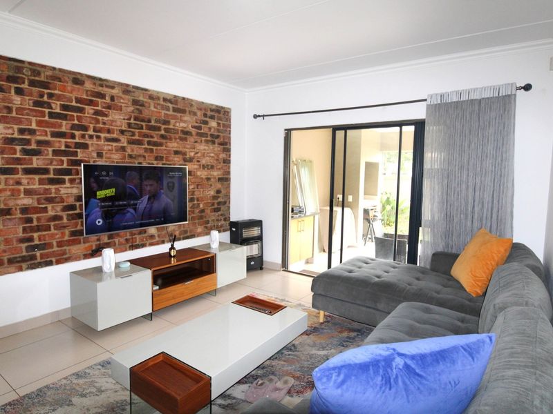 A well-lit living room featuring an exposed brick accent wall, tiled flooring, and large sliding glass doors providing access to the patio area.