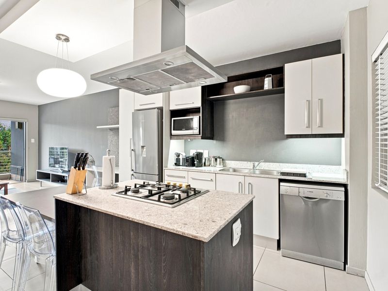 Modern open-plan kitchen featuring a central island with gas hob, stone countertops, integrated appliances, and sleek cabinetry, flowing into the living area.