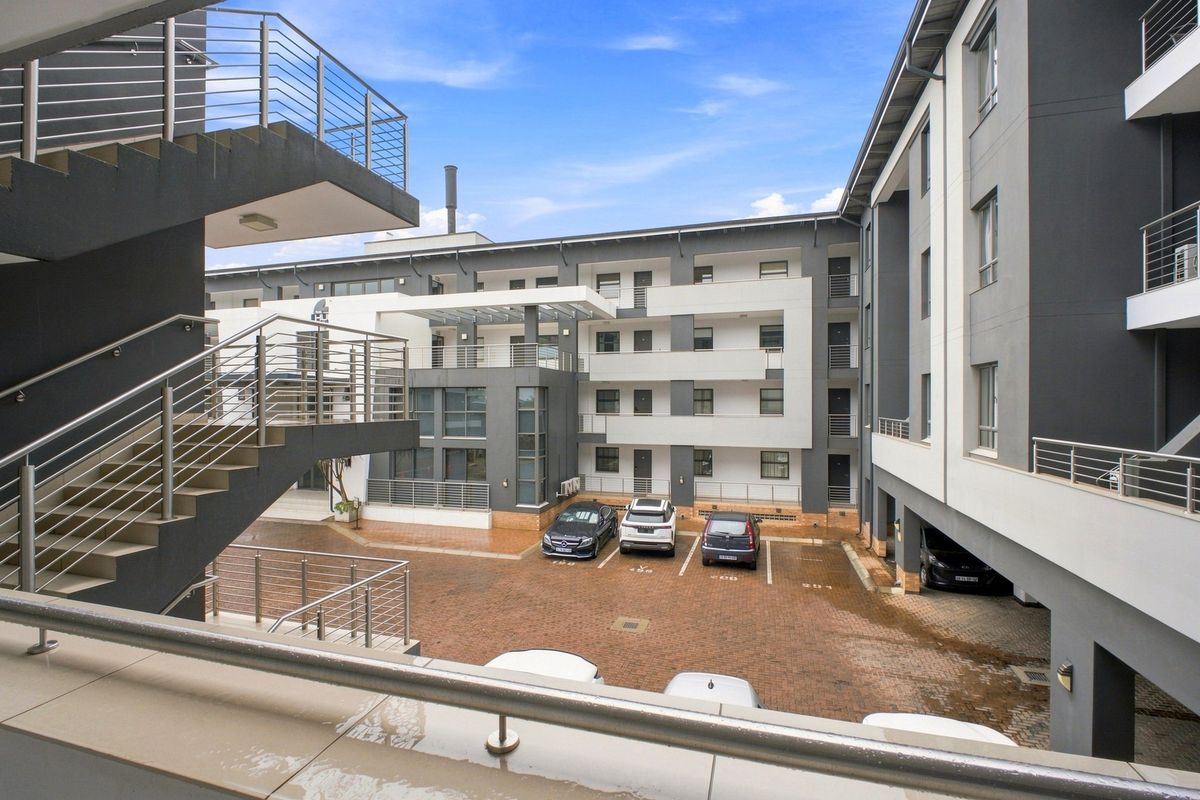 View of the apartment complex courtyard featuring paved parking areas, multi-level building facades, and external staircases with modern stainless steel railings.