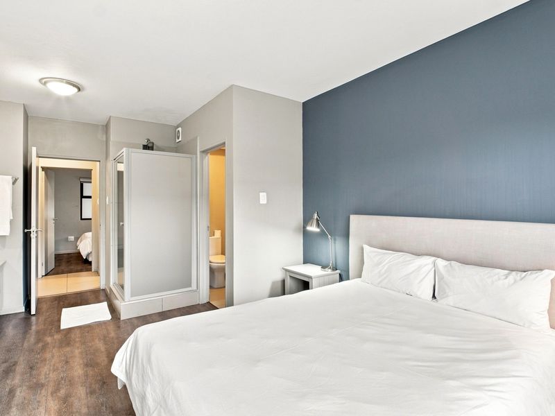A well-maintained bedroom featuring laminate flooring, a feature wall, and an en-suite bathroom with a shower cubicle and separate toilet area.