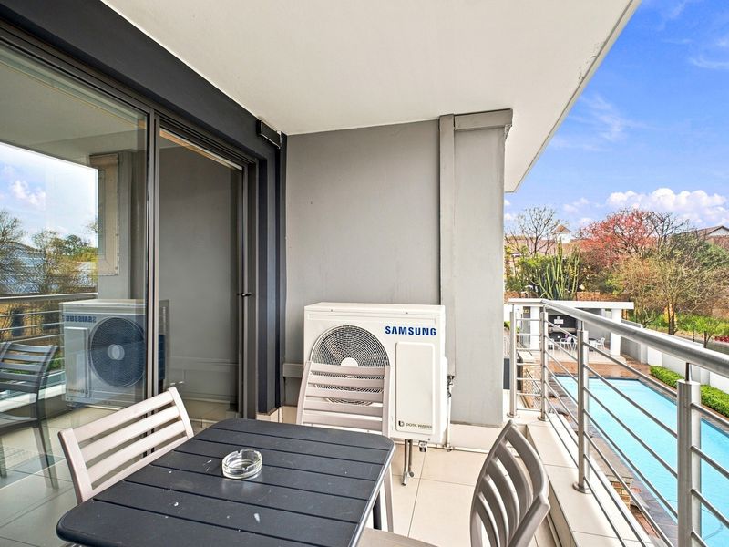 A covered balcony featuring tiled flooring, stainless steel railings, and a view overlooking the complex swimming pool area.