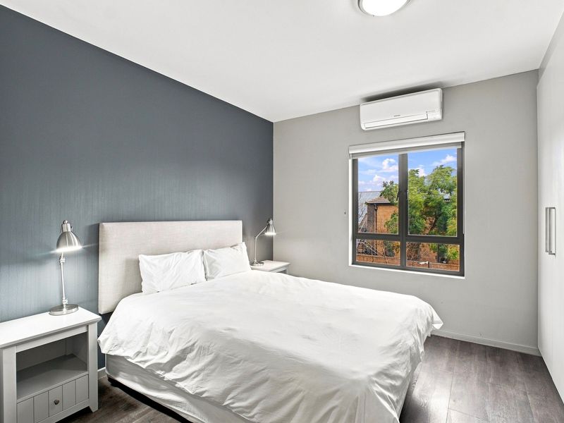 A well-maintained bedroom featuring a dark accent wall, split-system air conditioning, built-in wardrobe, and laminate flooring with a view through the window.