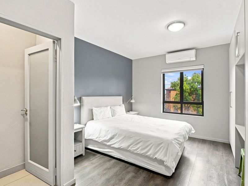 A well-maintained bedroom featuring laminate flooring, a built-in wardrobe, and a split-system air conditioner for climate control.