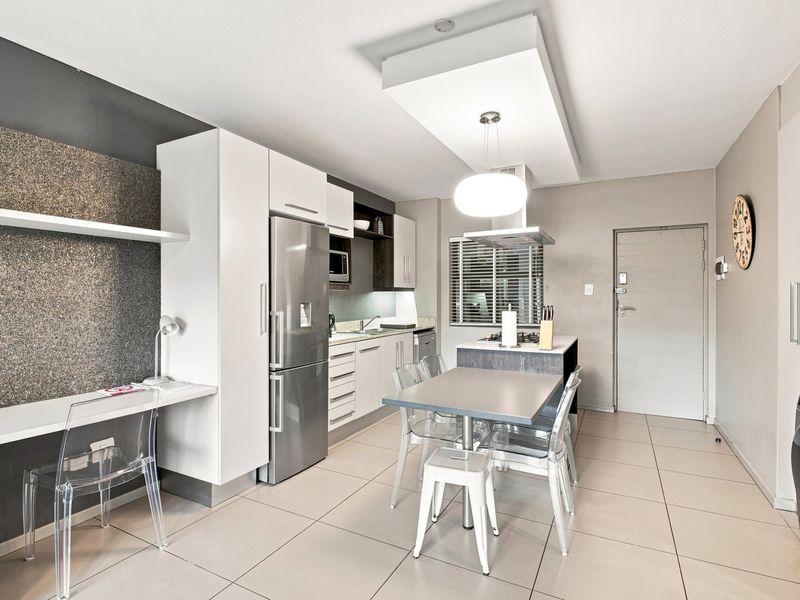 Modern open-plan kitchen and living area featuring sleek cabinetry, integrated appliances, tiled flooring, and a dedicated built-in workspace.