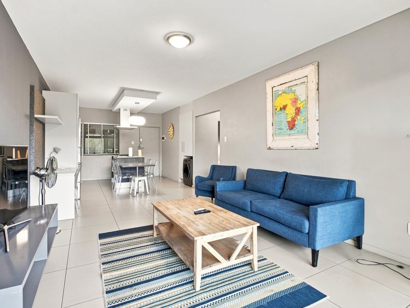 Open-plan living and kitchen area featuring neutral tiled flooring, modern recessed lighting, and a functional kitchen layout with integrated appliance space.