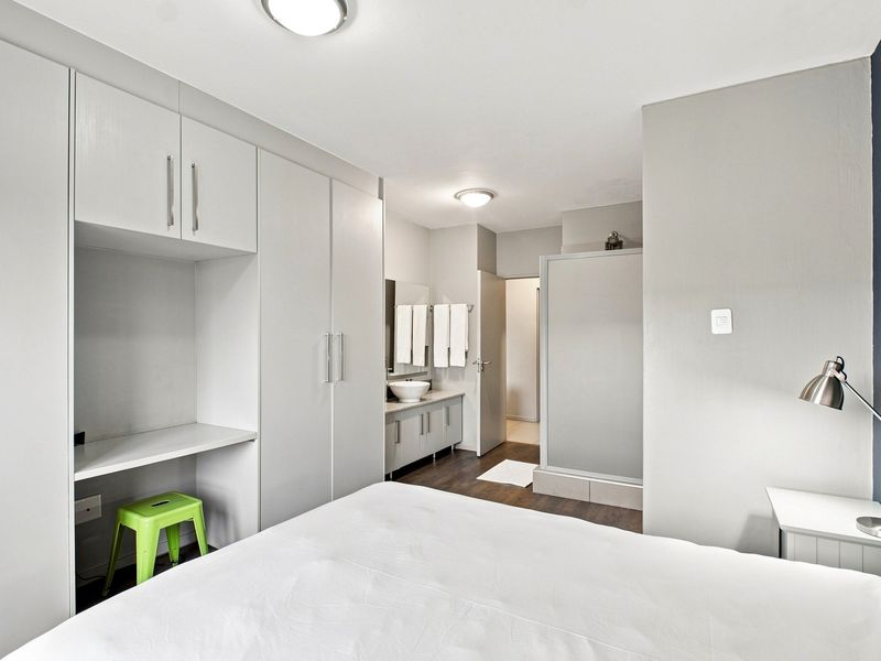 Modern bedroom featuring extensive built-in cupboards with an integrated desk and a convenient en-suite bathroom with a vanity basin and shower enclosure.