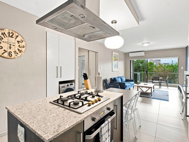 Modern open-plan apartment featuring a well-equipped kitchen with gas hob and island, flowing seamlessly into a living area with access to a private balcony.