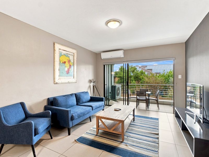 A bright living room featuring tiled floors, a split-system air conditioner, and large sliding glass doors that open onto a private balcony.