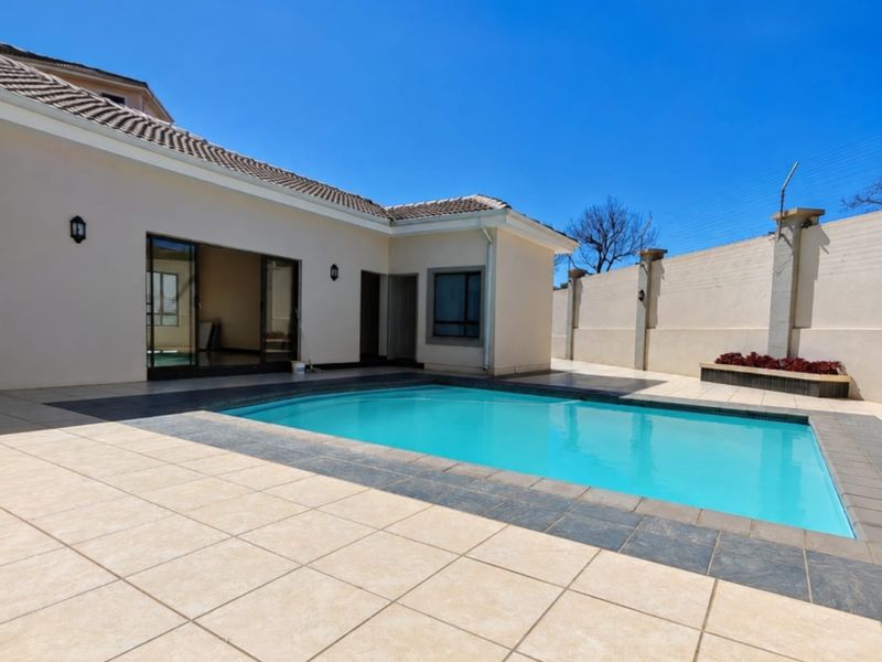 A well-maintained outdoor pool area featuring a tiled patio, clear swimming pool, and secure perimeter wall with electric fencing.