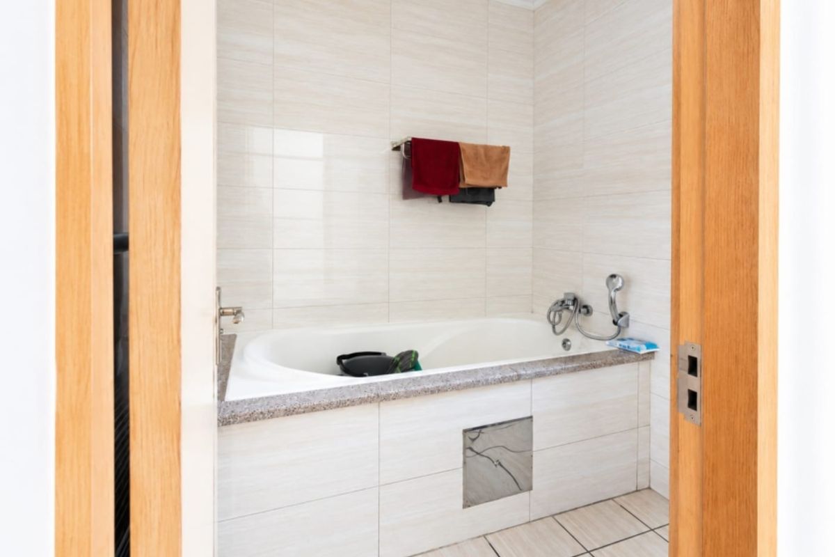 A clean bathroom featuring a built-in bathtub with granite surround, neutral ceramic wall and floor tiling, and chrome fixtures.