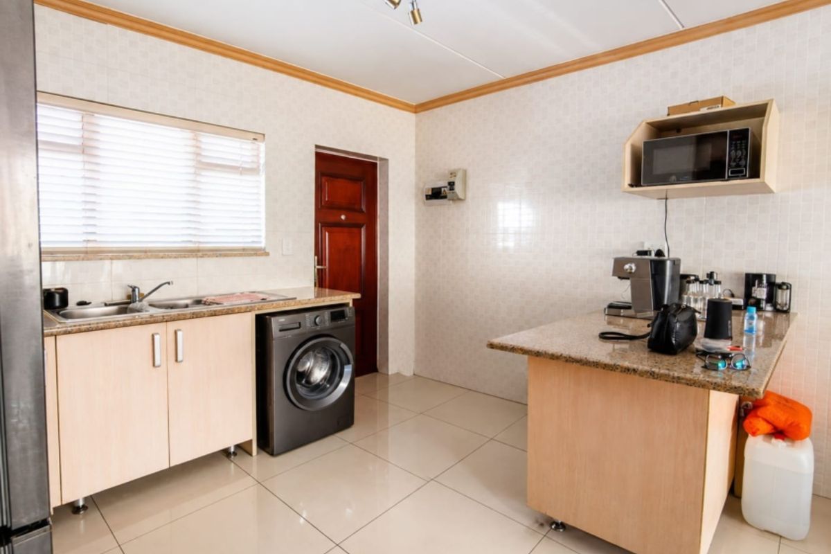 A functional kitchen featuring light wood cabinetry, granite countertops, tiled walls, and integrated laundry plumbing, offering a clean and practical workspace.