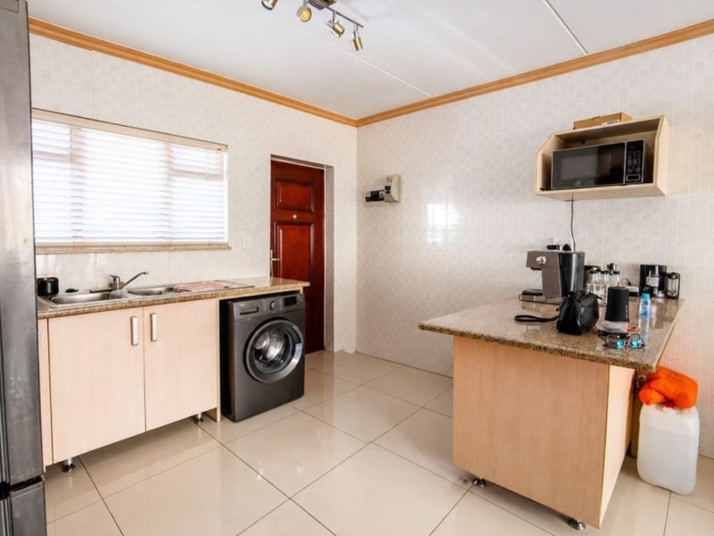 A functional kitchen featuring light wood cabinetry, granite countertops, tiled walls, and integrated laundry plumbing, offering a clean and practical workspace.