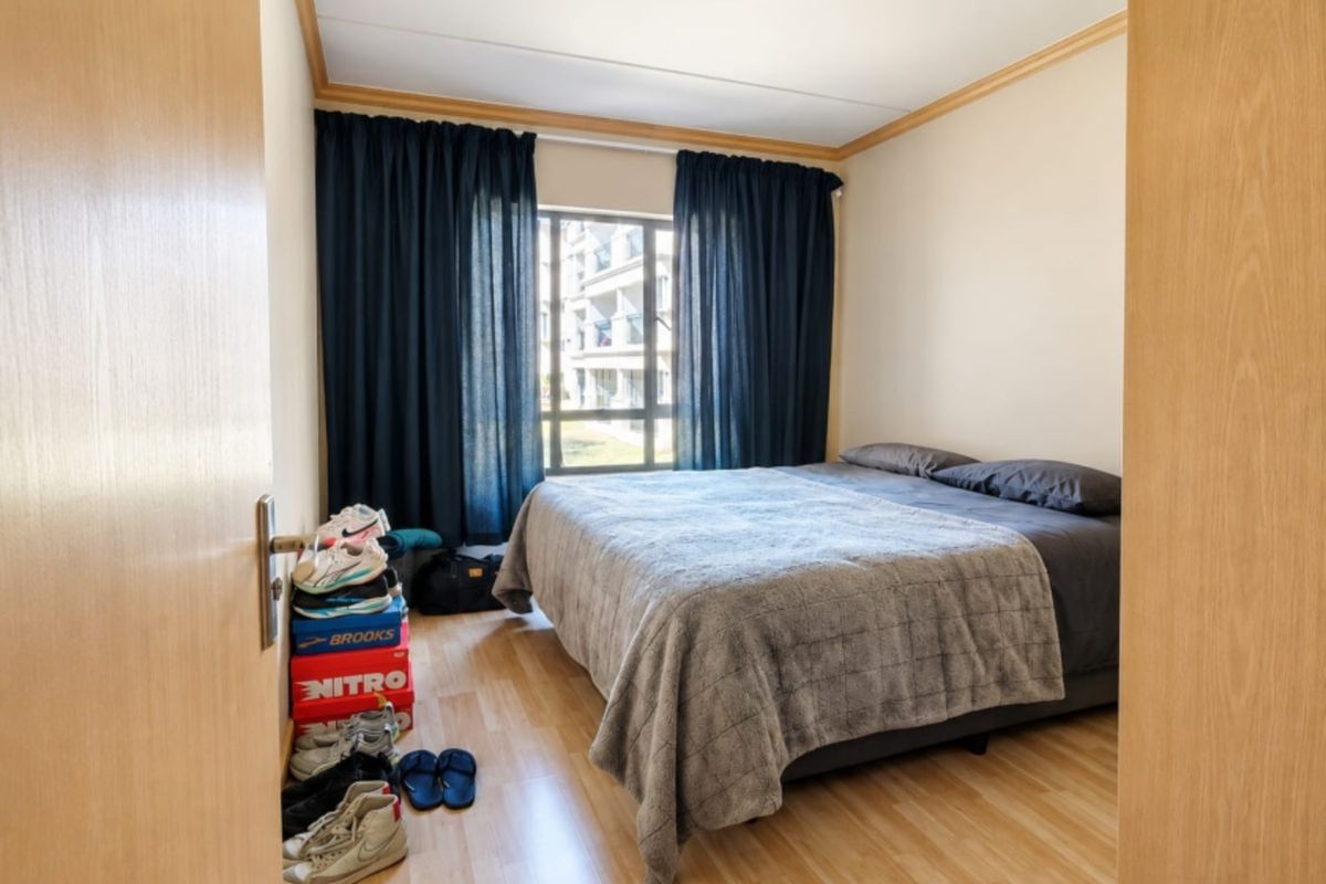 A functional bedroom featuring light-toned laminate flooring, a central ceiling light, and a window with dark curtains.