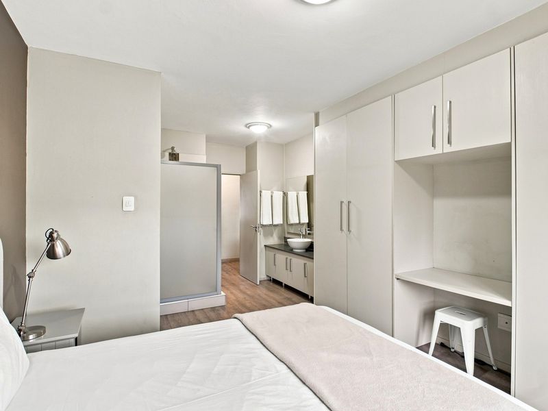 A well-maintained bedroom featuring built-in cupboards, a integrated desk area, and an en-suite bathroom with a shower and vanity basin.