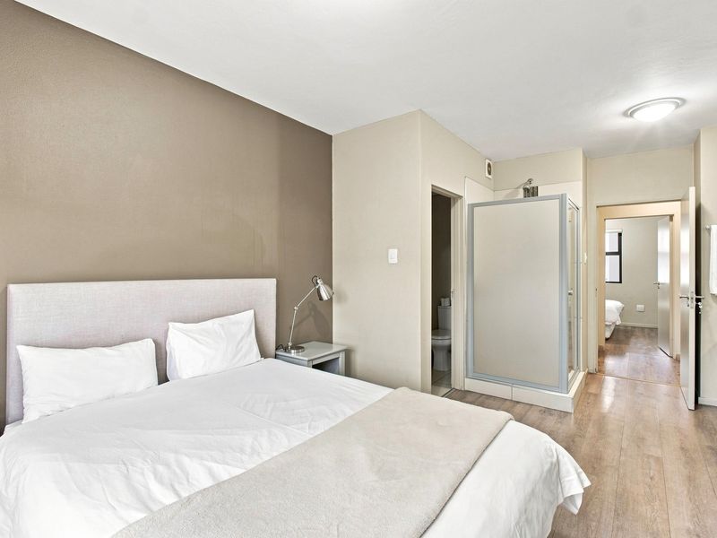 A well-maintained bedroom featuring laminate flooring, an integrated en-suite shower cubicle, and a separate toilet area.