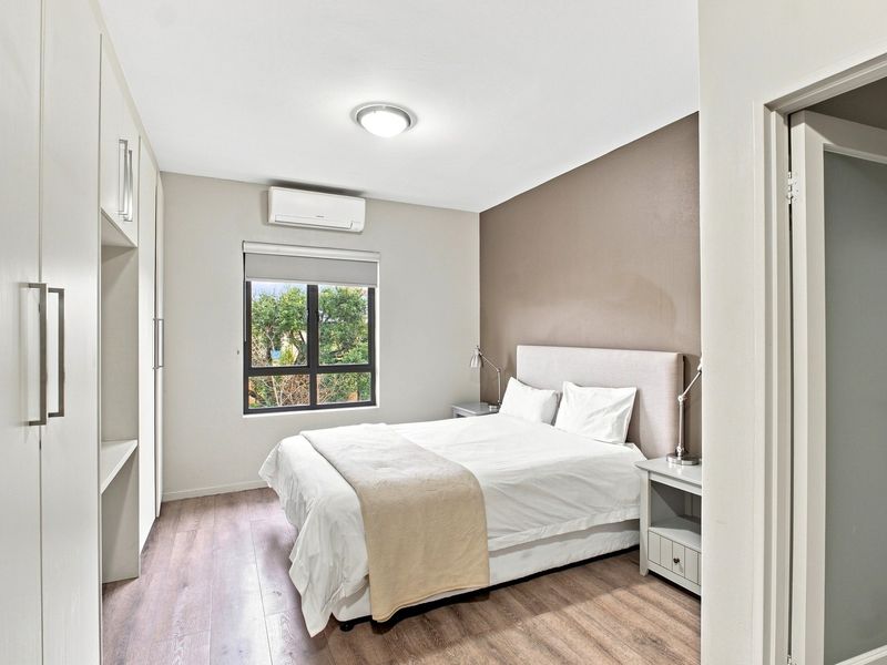 A well-maintained bedroom featuring laminate flooring, built-in cupboards, and a wall-mounted split-system air conditioner.