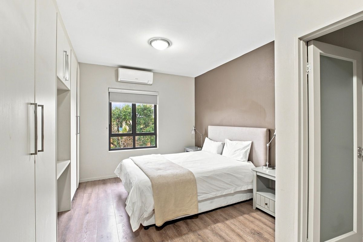 A well-maintained bedroom featuring laminate flooring, built-in cupboards, and a wall-mounted split-system air conditioner.