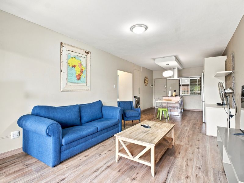 Open-plan living and kitchen area featuring modern laminate flooring, neutral walls, and a functional kitchen layout with built-in cabinetry and integrated appliances.