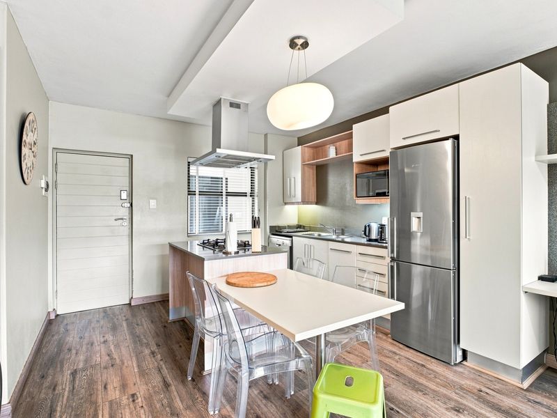 Modern open-plan kitchen and living area featuring sleek cabinetry, integrated appliances, a gas hob, and durable laminate flooring in a well-maintained apartment setting.