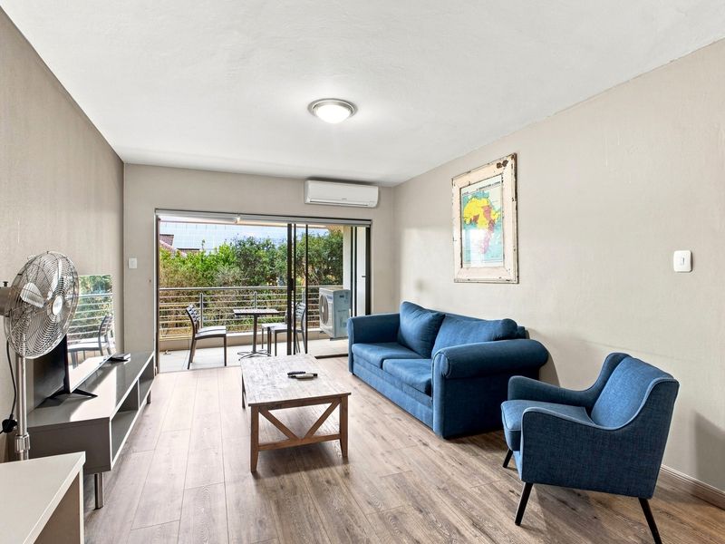 A bright living room featuring laminate flooring, a split-system air conditioner, and large sliding glass doors that open onto a private balcony.