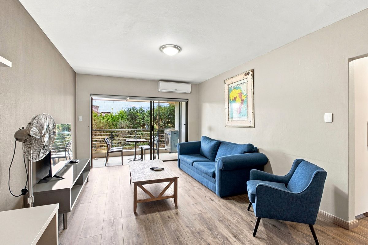 A bright living room featuring laminate flooring, a split-system air conditioner, and large sliding glass doors that open onto a private balcony.