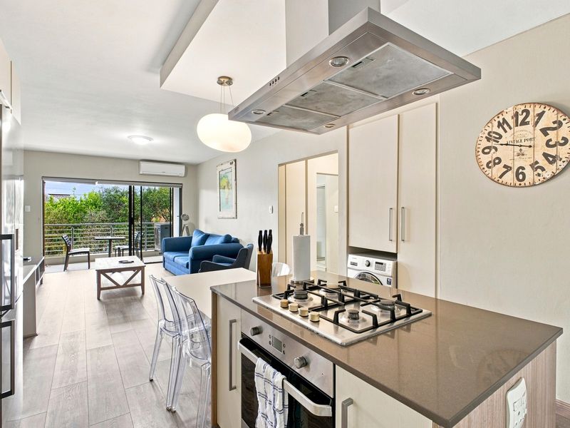 Modern open-plan kitchen and living area featuring stone countertops, gas hob, built-in oven, and seamless access to a private balcony.