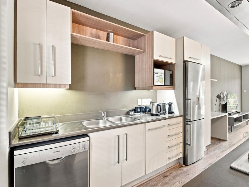 Modern kitchen featuring sleek built-in cabinetry, stainless steel appliances, integrated dishwasher, and durable laminate flooring, seamlessly flowing into the adjacent living area.
