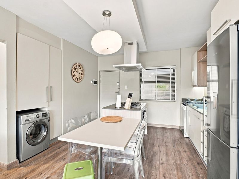 Modern kitchen featuring sleek cabinetry, integrated laundry space, laminate flooring, and a central island with a built-in hob and extractor fan.