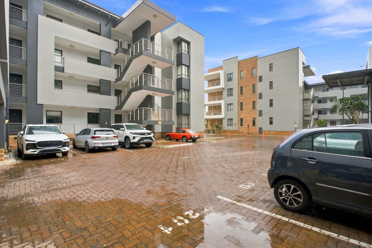 A view of the apartment complex exterior featuring a paved parking area, multi-story building facades, and external staircases.