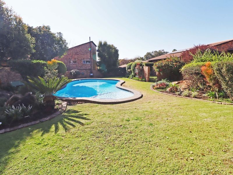 A well-maintained private garden featuring a swimming pool with paved surround, established landscaping, and brick boundary walls.