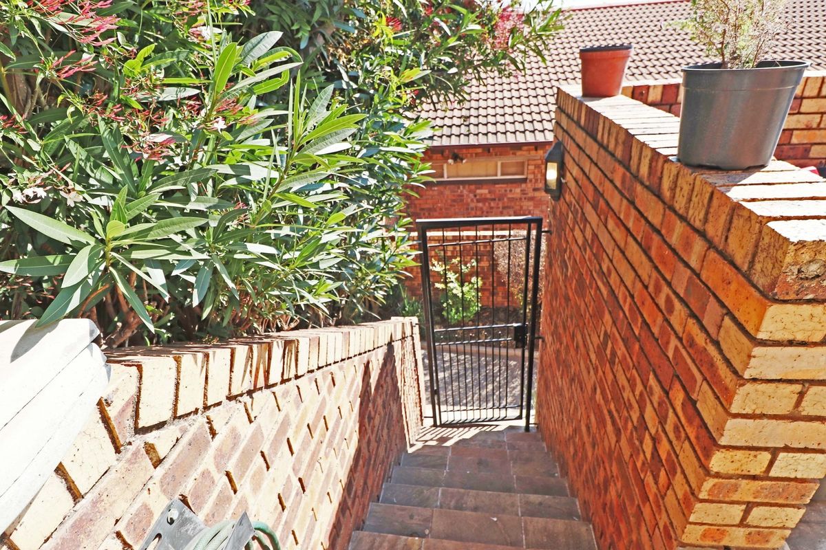 A brick-walled staircase leading down to a metal security gate, providing access to the rear exterior area of the property.