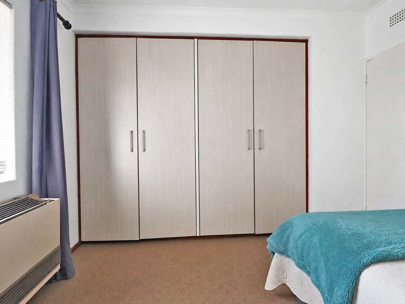 A bedroom featuring neutral built-in cupboards, carpeted flooring, and a ventilation grille, offering a functional and well-maintained living space.