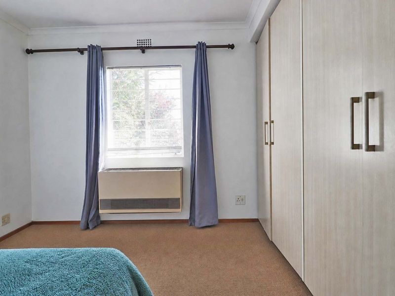 A bedroom featuring built-in cupboards, a window with curtains, and a wall-mounted air conditioning unit.