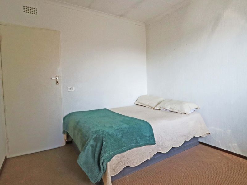 A simple bedroom featuring neutral walls, carpet flooring, and a ventilation grille.