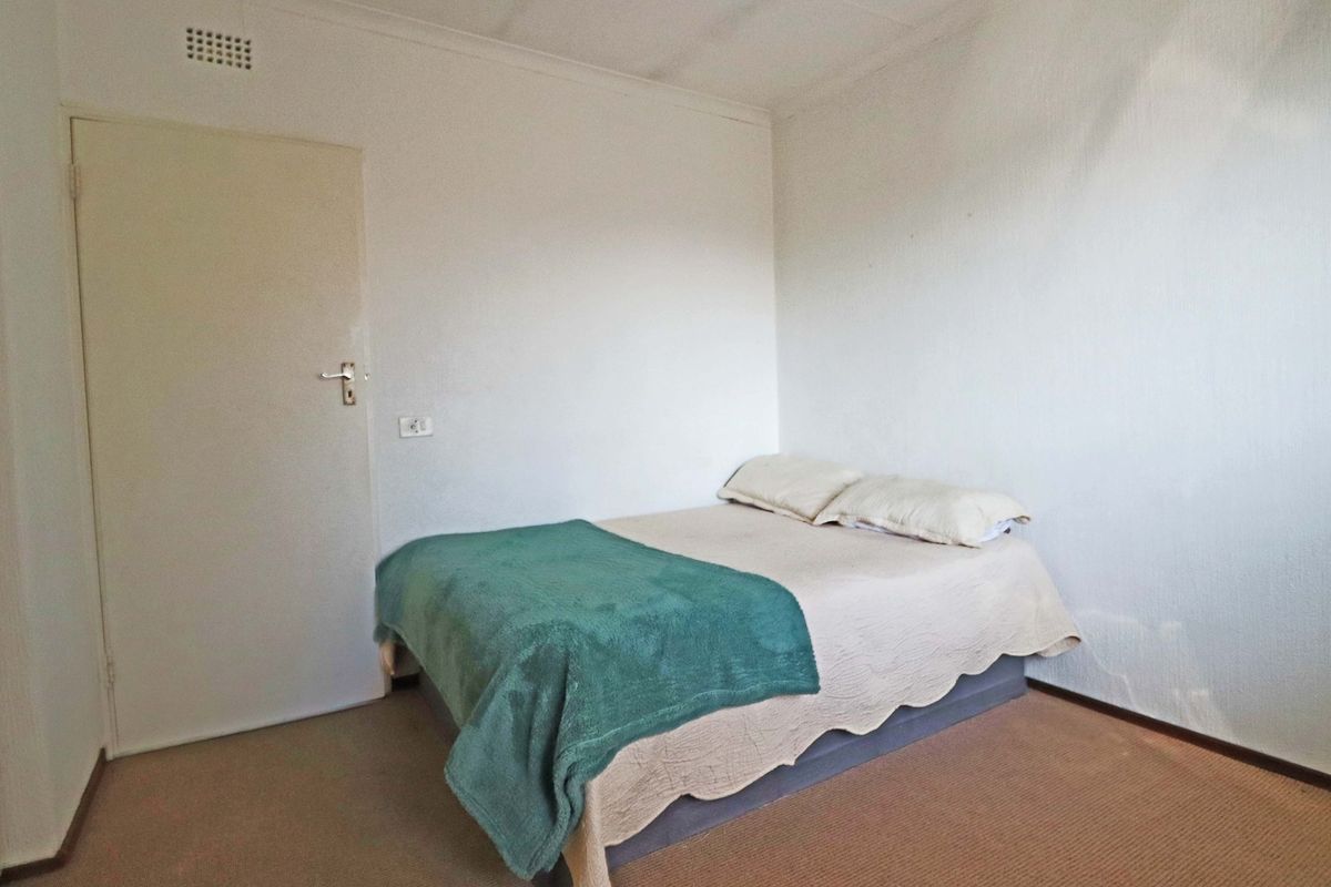A simple bedroom featuring neutral walls, carpet flooring, and a ventilation grille.
