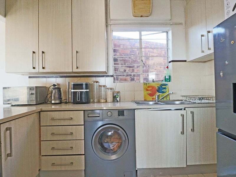 A functional kitchen featuring laminate cabinetry, tiled backsplash, double basin sink, and an integrated washing machine with security bars on the window.