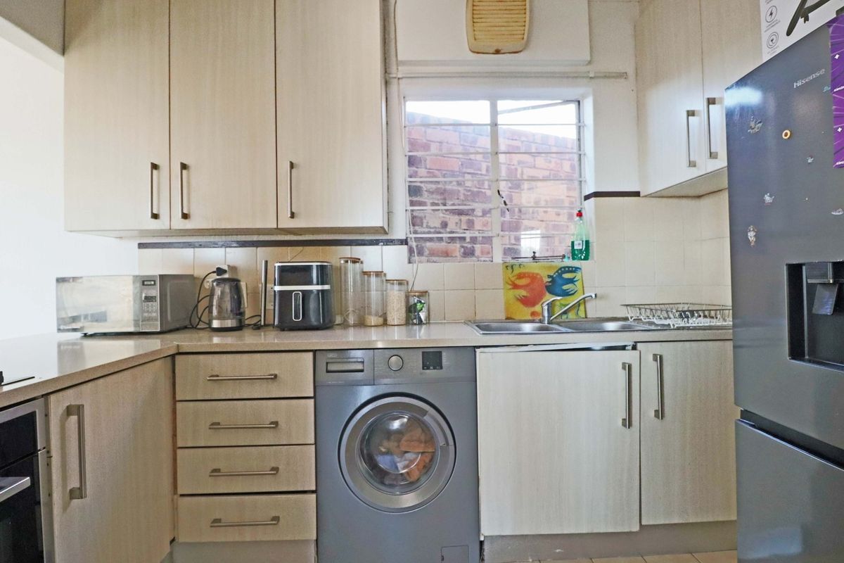 A functional kitchen featuring laminate cabinetry, tiled backsplash, double basin sink, and an integrated washing machine with security bars on the window.