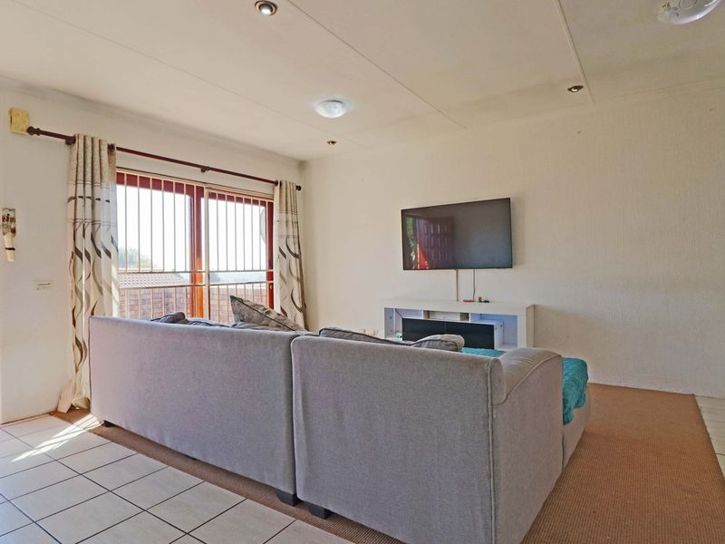 A living room featuring a mix of tiled and carpeted flooring, recessed lighting, and a sliding glass door with security bars leading to the exterior.