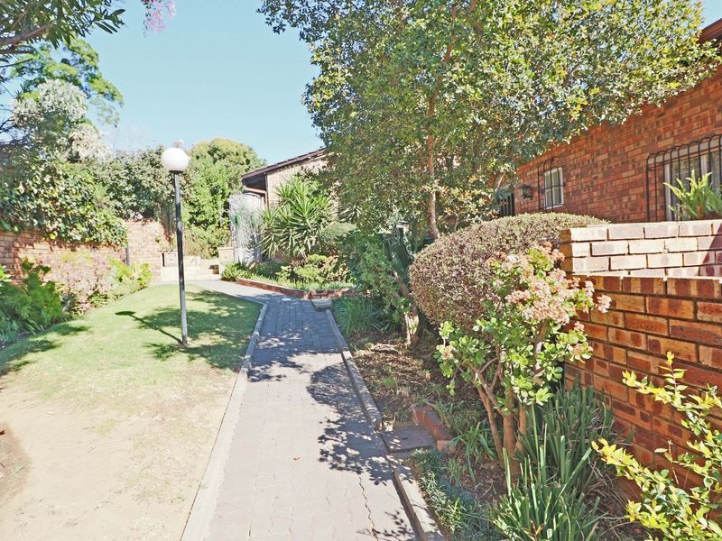 A private rear garden area featuring a paved walkway, established landscaping, and a brick boundary wall alongside the apartment building facade.