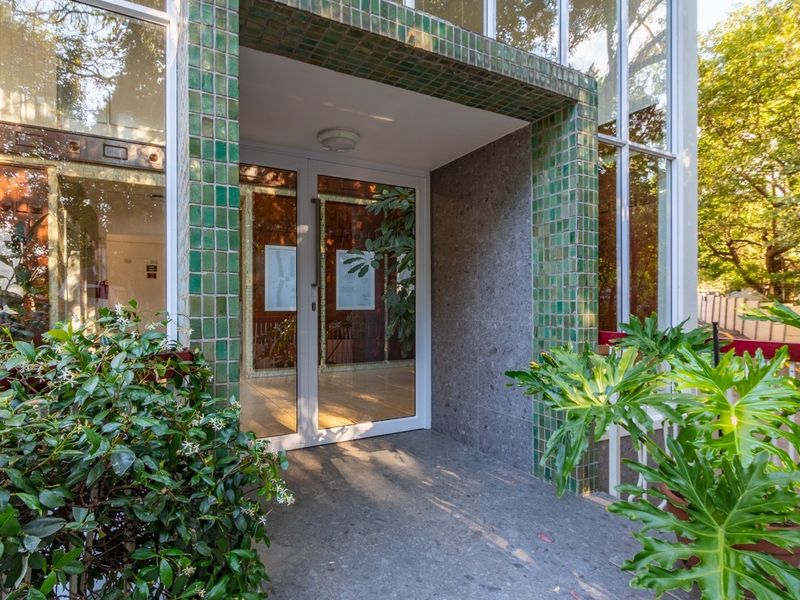 Main building entrance featuring a distinctive green ceramic tile facade, glass double doors, and stone flooring, providing a bright and welcoming access point.