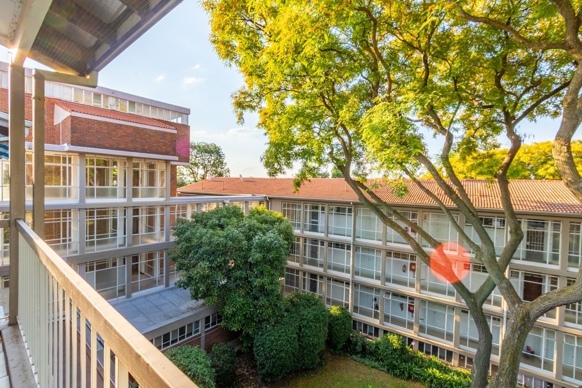 View from a balcony overlooking a well-maintained apartment complex courtyard with mature trees and brick building architecture.