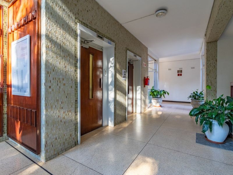 A well-maintained apartment building hallway featuring elevator access, mosaic tiled walls, and durable terrazzo flooring.