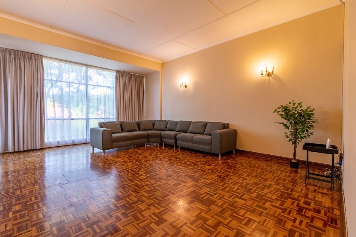 Spacious living room featuring classic parquet flooring, warm wall sconce lighting, and a large window providing ample natural light.
