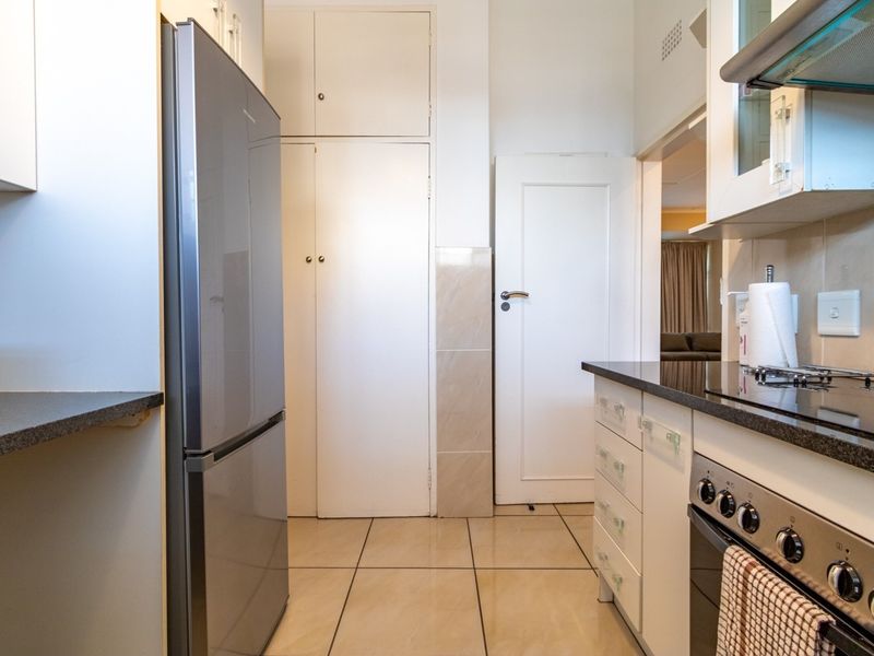 A functional kitchen featuring built-in cabinetry, granite countertops, an electric oven with hob, and tiled flooring with ample storage space.