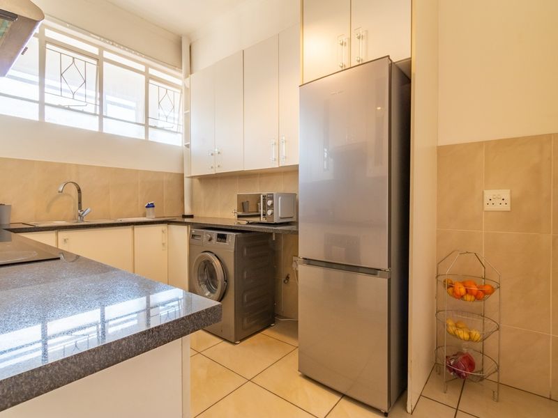A functional kitchen featuring granite countertops, ample built-in cabinetry, tiled backsplash, and a dedicated space for laundry appliances.