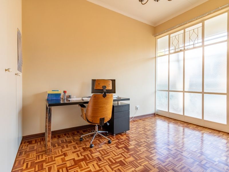 A bright home office featuring classic parquet flooring and a large glass partition wall, providing a functional and well-lit workspace.