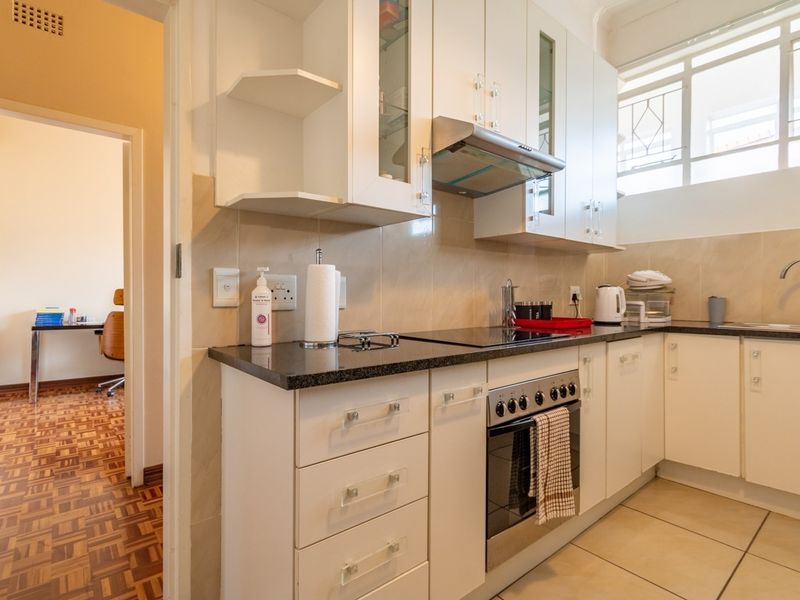 A functional kitchen featuring white cabinetry, granite countertops, a built-in oven with hob, and a tiled backsplash, with an adjacent view into another room.