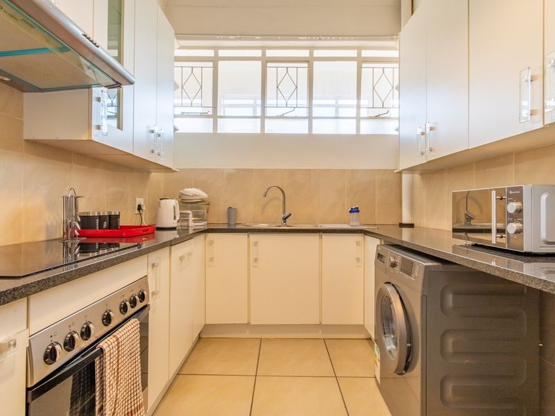A functional galley-style kitchen featuring white cabinetry, granite countertops, tiled backsplash, integrated stove, and space for a washing machine.