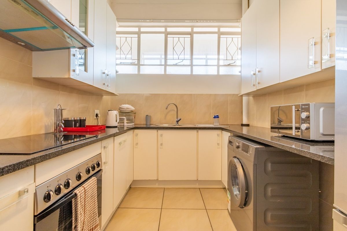 A functional galley-style kitchen featuring white cabinetry, granite countertops, tiled backsplash, integrated stove, and space for a washing machine.